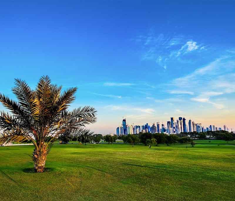 Al Bidda Park in Doha with green lawns, walking paths, and city skyline in the background on a sunny day.