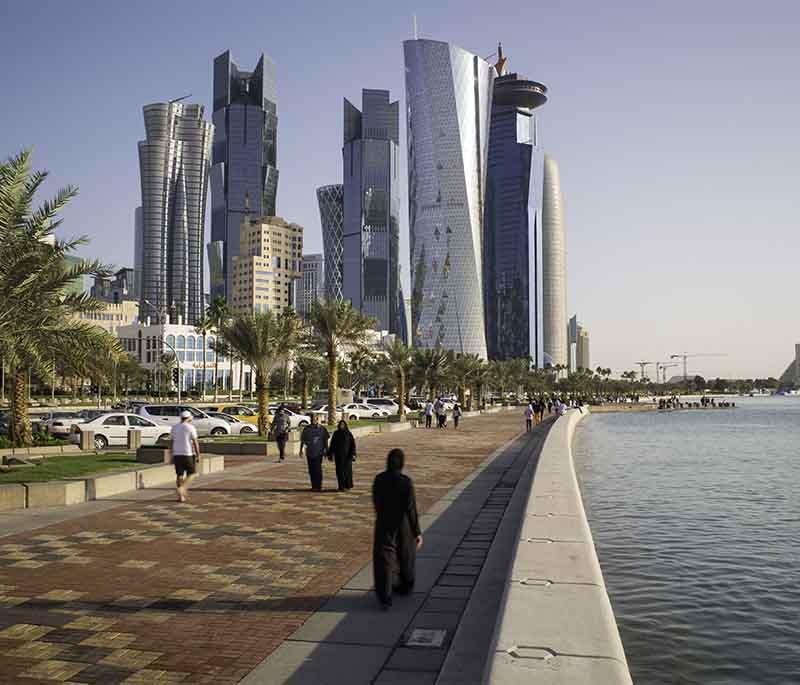 Bustling street scene in Al Doha Al Jadeda showing shops, moving traffic, and pedestrians under clear daylight skies.