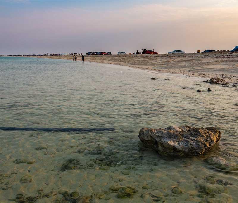 Peaceful shoreline at Al Nouf Beach with golden sand, clear blue water, and gentle waves under a sunny sky.