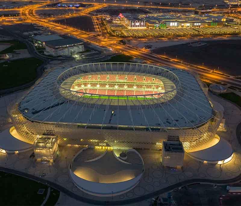 Modern Al Rayyan Stadium with unique design and glowing lights, set against the evening sky during a sports event.