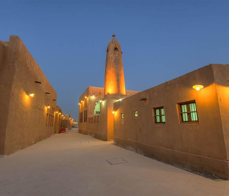 Traditional architecture at Al Wakrah Souq with wooden beams, lanterns, and people strolling through open-air alleys.