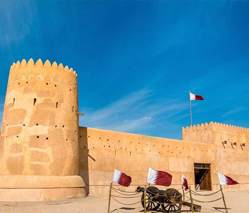 Historic Al Zubara Fort with sandy-colored walls, watchtowers, and desert surroundings under a bright blue sky.