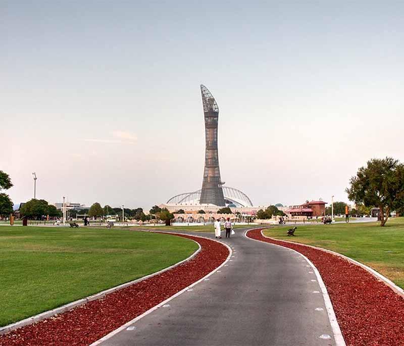 Families walking through Aspire Park with green lawns, fountains, and the city skyline in the background.