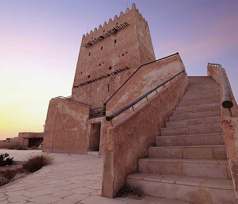 Barzan Towers rising above the desert, showing historic Qatari watchtowers with stone walls and blue sky above.