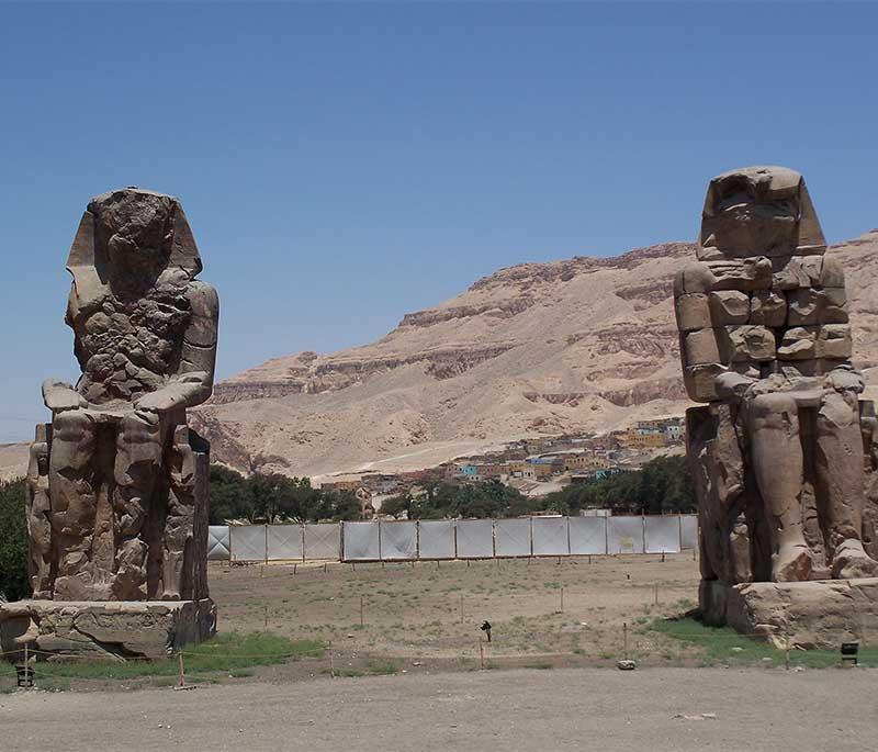 Colossi of Memnon, two massive stone statues of Pharaoh Amenhotep III, standing guard at the entrance of his mortuary temple.