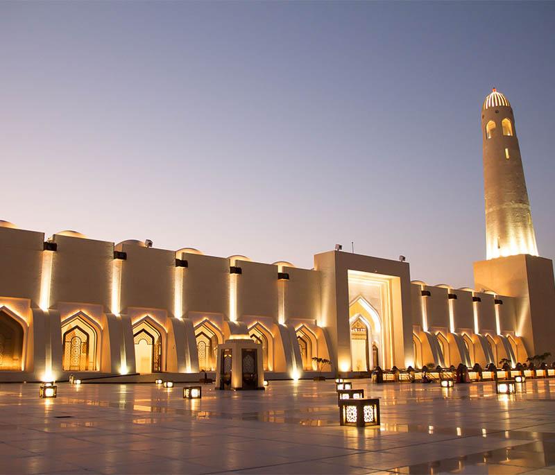Doha Opera House with elegant columns, ambient lights, and guests arriving for a performance in the evening.