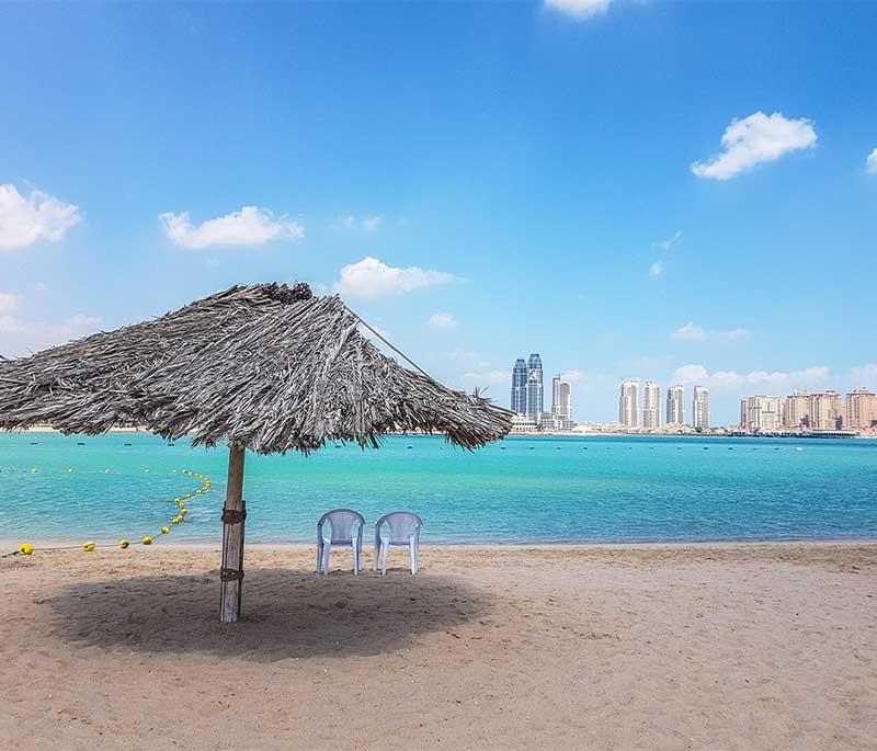 Sandy Katara Beach with sunbathers, umbrellas, and calm waters stretching toward the horizon under clear skies.