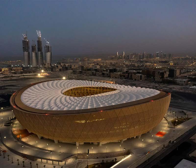 Grand Lusail Iconic Stadium with golden lattice exterior, dramatic lighting, and fans arriving for an event.
