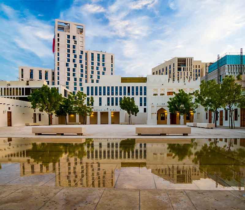 Msheireb Museums' restored heritage houses with Qatari architecture, palm trees, and visitors walking nearby.