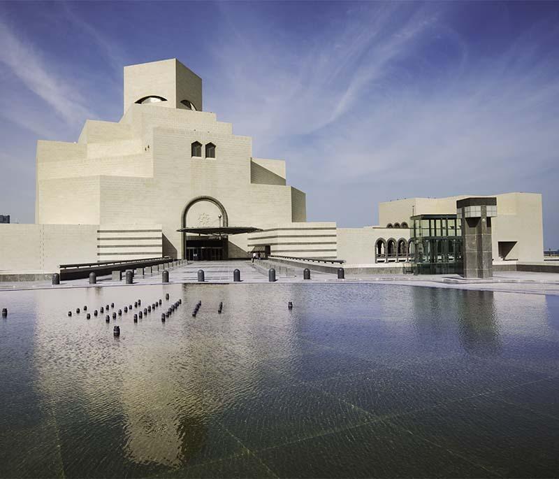 Museum of Islamic Art with geometric white facade, set against the Doha skyline and reflecting pool at sunset.