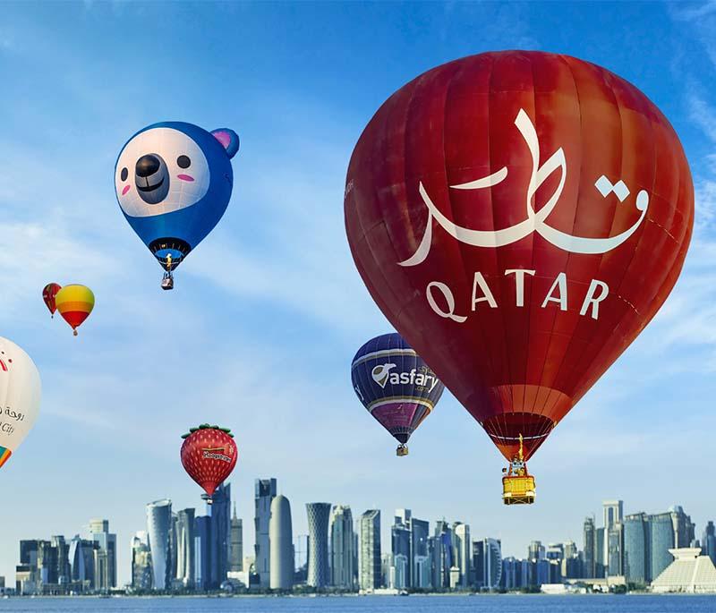 Colorful hot air balloons rising over the desert during Qatar Ballooning, with golden dunes and clear skies.