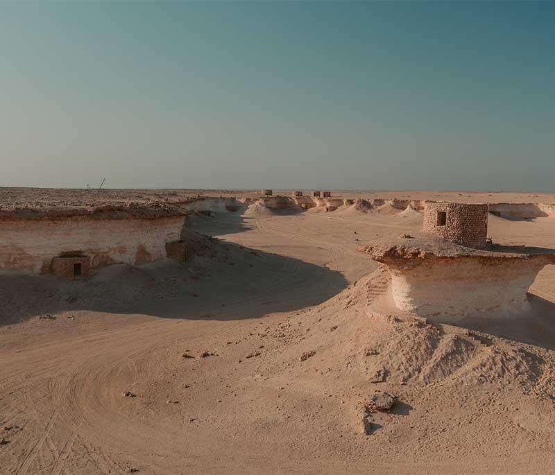 Dramatic rock formations at Ras Abrouq Desert with cliffs, open sand, and vast skies in the natural reserve.
