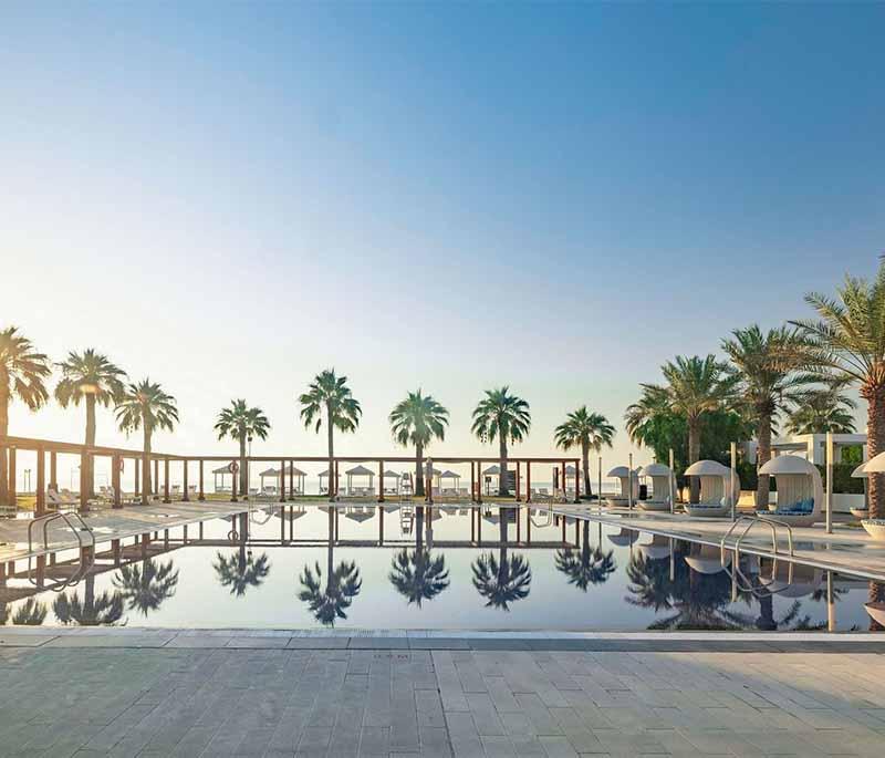 Beachfront at Sealine Beach Resort with umbrellas, resort guests, and calm blue waters under sunny weather.